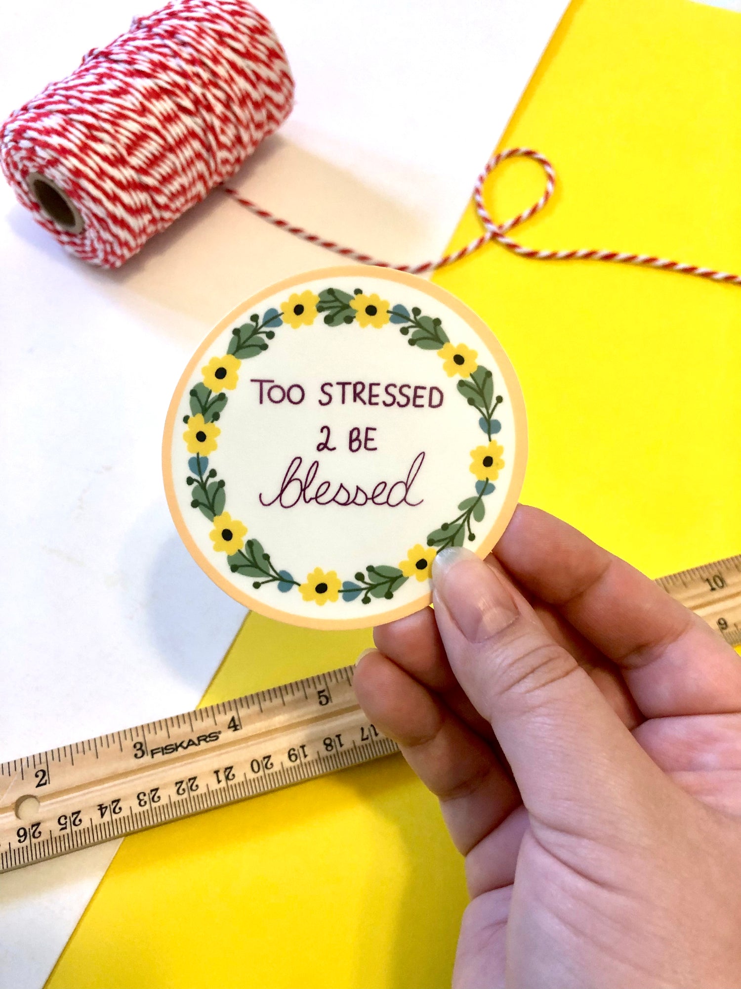 hand holding a sticker of cross stitch artwork that reads "too stressed 2 be blessed"